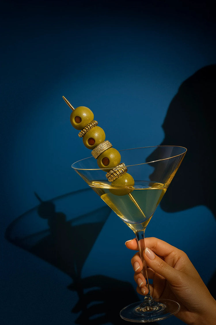 Hand holding a martini glass with olives on a skewer against a blue background